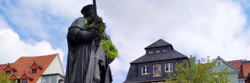 In Jena ist es Brauch, dass frischgebackene Doktor*innen einen Kranz über das Schwert vom Hanfried (Statue von Johann Friedrich I. von Sachsen, dem Begründer der Universität) auf dem Marktplatz werfen.(Das Foto zeigt einen Kranz, der in die Höhe geworfen wird und sein Ziel hoffentlich nicht verfehlt.