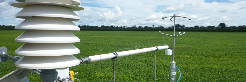 Eddy-Covarianz-Messung über Soja in Tanguro, Brasilien an einem heiteren Tag.
Im Vordergrund links eine weiße Wetterhütte für einen Temperaturfeuchte Sensor, in der Mitte das Ansaugrohr für Luft, die zum Gasanlysator geleitet wird und direkt daneben dem Ansaugtrichter das 3D Anemometer zur Bestimmung der Windrichtung. Im Hintergrund ein riesiges hellgrünes gelbblühendes Sojafeld, das am Horizont von Wald eingesäumt wird.
