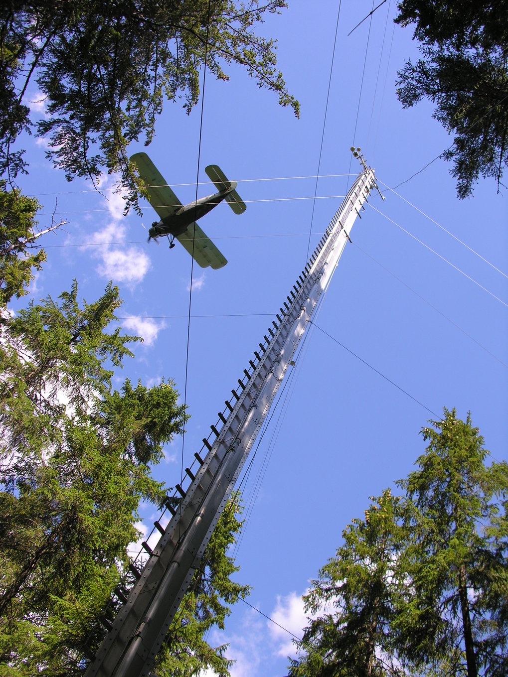 Antonov Flugzeug, wie es gerae am John Byers Turm in Federovskoje vobeifliegt. Foto vom Boden gen Himmel . Inder Mitte der Messturm und links davon das Flugzeug.