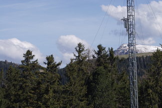 Eddy-Corarianz-Turm in Renon - Italien, während des Advex-Experimentes. Teil eines Gittermast am rechten Bildrand mit etlichen ABspannungen. vor einem Fichtenwald im Gebirge. Ein Schneebedeckter Berg im Hintergrund. Gro0e weisse Wolken am hellblaverschleiertem Himmel.