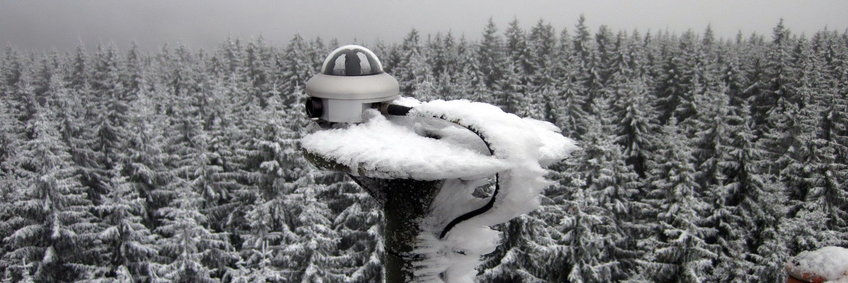 Sunshine pyranometer SPN1 on top of the measuring tower at Wetzstein (© K. Hippler/BGC) Iced sunshine pyranometer SPN1 in front of snow-covered spruces at Wetzstein (Thuringian Slate Mountains), gray sky in the background. The ice has grown with the wind direction and has beautiful bizarre shapes. One could believe it is a black-and-white picture. However, at the lower right edge of the picture you can see a very small red part of the measuring tower.