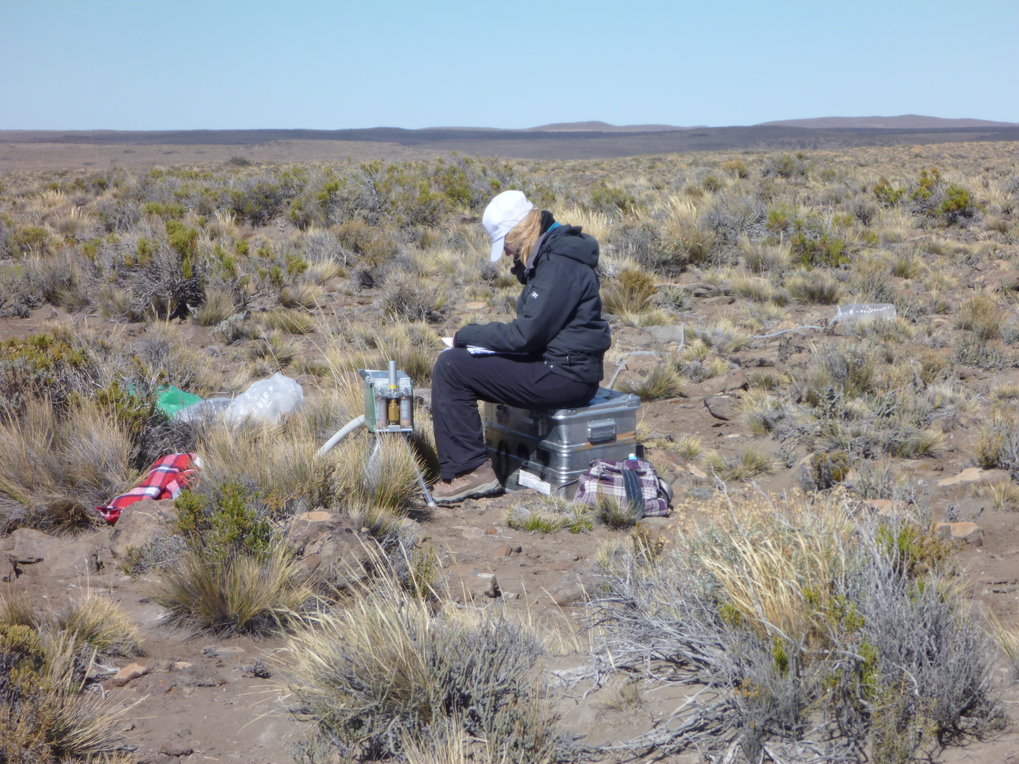 Wissenschaftlerin sitzt auf Zarges-Box umgeben von Material zur Probennahme auf einem Hochplateau in Argentinien.