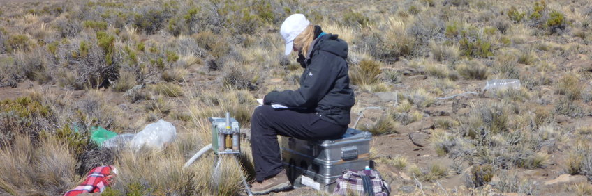 Wissenschaftlerin sitzt auf Zarges-Box umgeben von Material zur Probennahme auf einem Hochplateau in Argentinien.