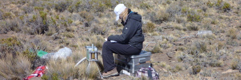 Scientist sitting on Zarges box surrounded by material for soil sampling on a high plateau in Argentina.