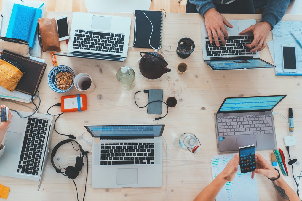 Arbeitstisch mit mehreren Laptops, Teekanne, Handy, Kopfhörer, Powerbank...