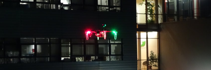 In the background the partially illuminated institute building, in the foreground a colorfully illuminated research drone.