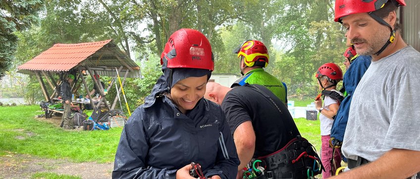 Mitglieder des Kurses für Seilklettertechnik in einer Zwangspause, während eines Regengusses, alle Personen in Klettergurten und mit Helm.