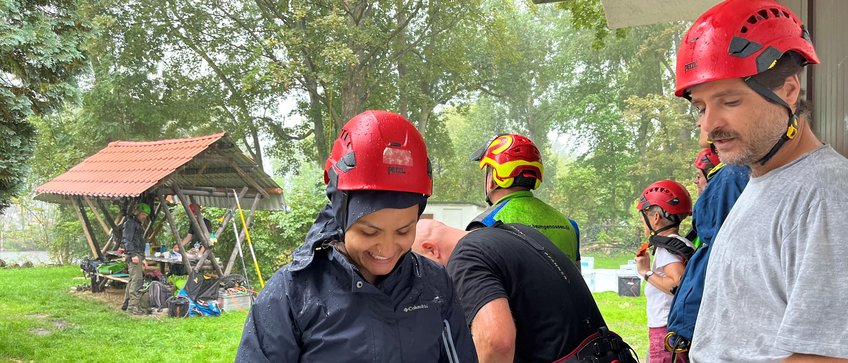 Members of the rope climbing technique course during a forced break, during a downpour, all people in harnesses and helmets.