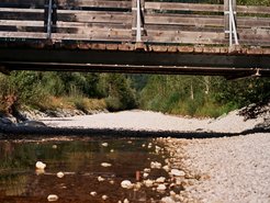 View of a wooden bridge spanning a partially dried out riverbed, exposing the rocky riverbed.