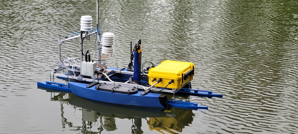 Zu sehen ist das sogenannte Minerva-Blueboat, eine  automatisierte Schwimmkammer für Gasaustauschmessungen auf Seen und Flüssen, entwickelt für das Projekt Q-Arctic. Es besteht aus mehreren blauen und grauen Schwimmkörpern, auf denen an einem Alugestänge, eine automatisierte Kammer und diverse Sonden und Messtechnik für Gasauschmessungen und Meteorologie verbaut sind.